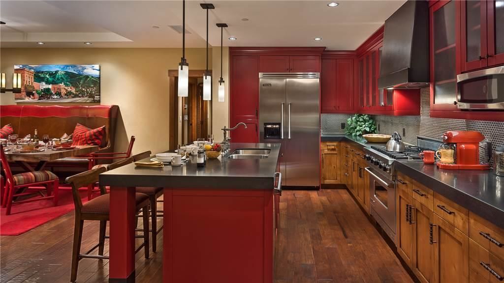 A modern kitchen with a central island, stainless steel appliances, and red cabinetry.