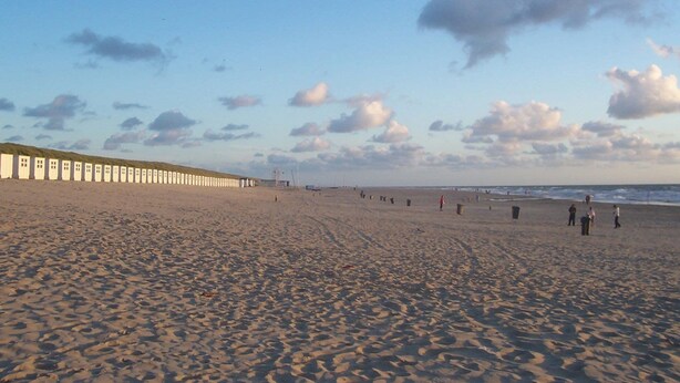 Uma extensa praia de areia com uma fileira de cabanas brancas à esquerda.