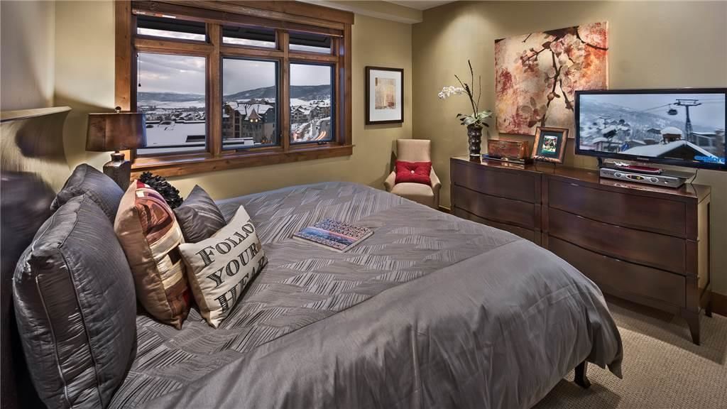 Un dormitorio con una cama grande, un aparador, un televisor y una ventana con vistas a un paisaje nevado.