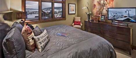 Un dormitorio con una cama grande, un aparador, un televisor y una ventana con vistas a un paisaje nevado.