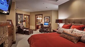 A hotel room with a large bed, a desk with a computer, a chair, a TV, and a dresser.
