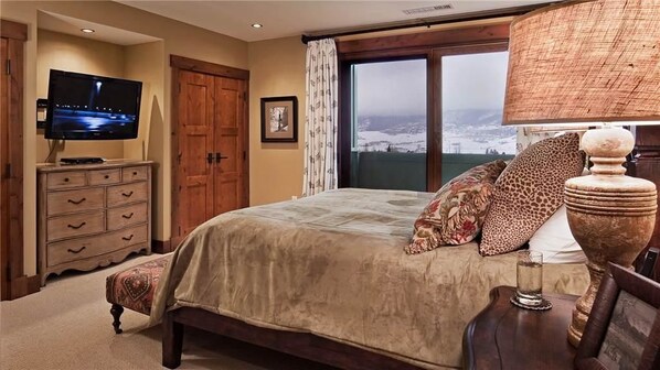 A bedroom with a large bed, a television on a dresser, a window with a view, and a lamp.