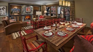 A dining area with a wooden table set for four, surrounded by red chairs. A fireplace is visible in the background, and there are framed pictures on the walls. - Moose Mountain 604 4 BedroomCondo By Moving Mountains (Steamboat Springs)