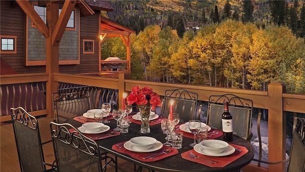 A dining table set for six with red placemats, white plates, and a bottle of wine.
