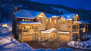 A large, multi-story lodge with a snow-covered roof, multiple balconies, and a well-lit entrance.