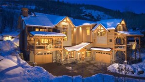 A large, multi-story lodge with a snow-covered roof, multiple entry points, and a well-lit exterior.
