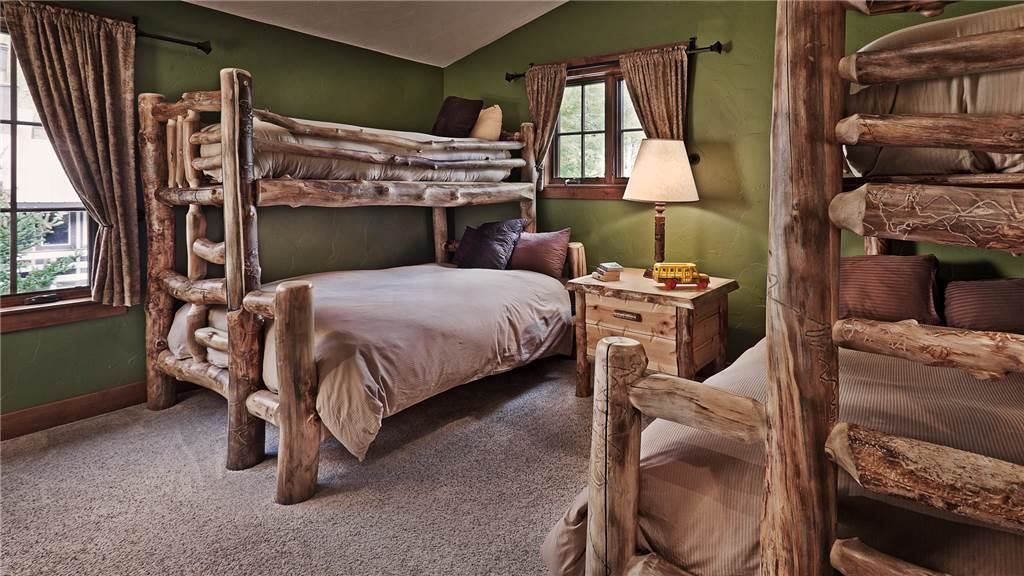 Un dormitorio rústico con una cama litera, una mesita de noche de madera y una ventana con cortinas.