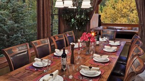 Comedor con una mesa de madera dispuesta para seis personas, rodeado de sillas de cuero y vista a árboles a través de una ventana.