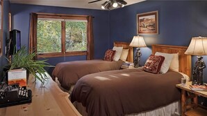 Een kamer met twee bedden, een houten bureau met telefoon, een plant en een raam met gordijnen.