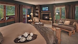 Een ruime slaapkamer met een groot bed, een open haard, een televisie en een balkon met houten spijlen.