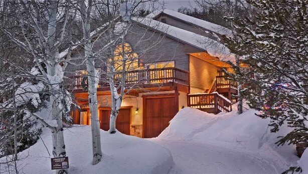 Een besneeuwde lodge met een houten gevel, een balkon en een trap naar de ingang.