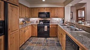 A kitchen with wooden cabinets, a black stove, a microwave, and granite countertops. - Argentiere 341 3 BedroomCondo By Moving Mountains (Steamboat Springs)