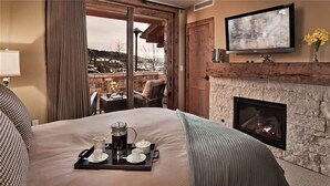 Une chambre d’hôtel avec un grand lit, une cheminée, une télévision et un balcon donnant sur l’extérieur.