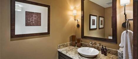 A bathroom with a large mirror, framed artwork, a sink, and a towel rack.