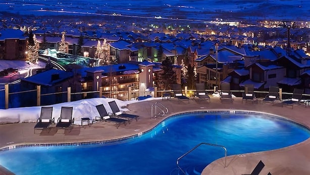 A swimming pool with lounge chairs and a view of snow-covered buildings at night. - Skyfall Ridge 702 2 BedroomCondo By Moving Mountains (Steamboat Springs)