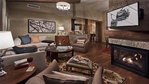 A spacious living room with a fireplace, comfortable seating, a coffee table, and a television mounted on the wall. - Skyfall Ridge 702 2 BedroomCondo By Moving Mountains (Steamboat Springs)