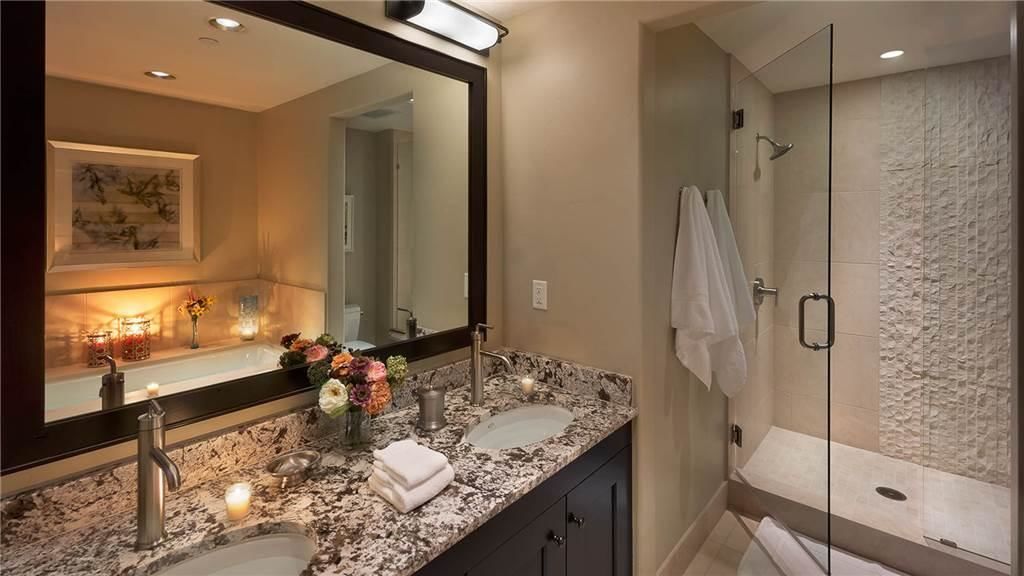 Un baño moderno con encimera de granito, dos lavamanos, un espejo grande y ducha con mampara de vidrio.