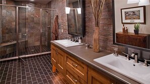 Un baño moderno con dos lavamanos, cabina de ducha de vidrio, armarios de madera y un espejo grande.