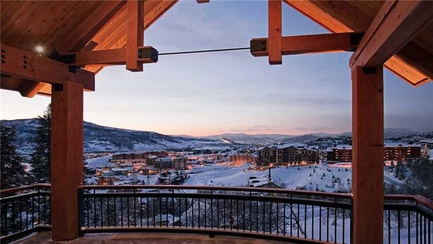 A wooden balcony with a view of a snow-covered landscape and buildings in the distance.