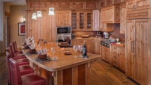 A spacious kitchen with wooden cabinets, a central island with bar seating, and modern appliances. - Falconhead Lodge North 5 BedroomHoliday home By Moving Mountains (Steamboat Springs)