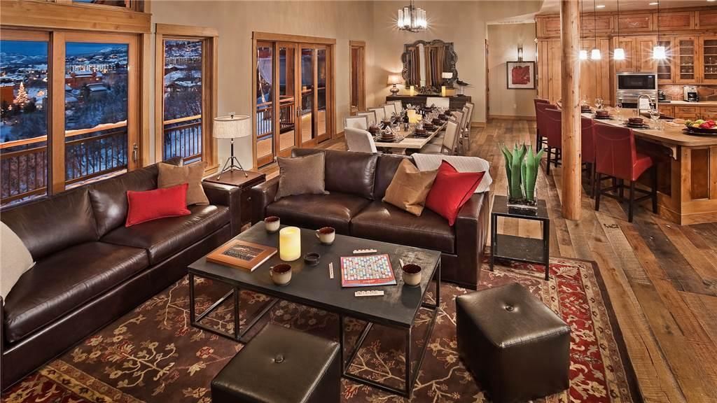 A cozy living room with a leather sofa, a coffee table, and a view of a snowy landscape through large windows.