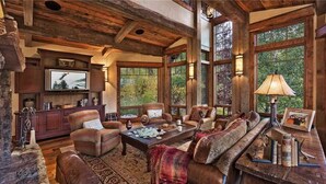 A rustic interior with a large wooden ceiling, comfortable seating, a fireplace, and large windows offering a view of the outdoors. - Gold Mine Lodge 6 BedroomHoliday home By Moving Mountains (Steamboat Springs)