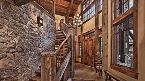 A rustic interior with a stone wall, wooden staircase, and large windows. - Gold Mine Lodge 6 BedroomHoliday home By Moving Mountains (Steamboat Springs)