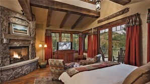 A cozy bedroom with a stone fireplace, a television, a large bed, and a balcony with red curtains. - Gold Mine Lodge 6 BedroomHoliday home By Moving Mountains (Steamboat Springs)