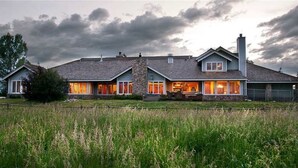 Une maison à deux étages avec une cheminée en pierre, de grandes fenêtres et une pelouse bien entretenue.