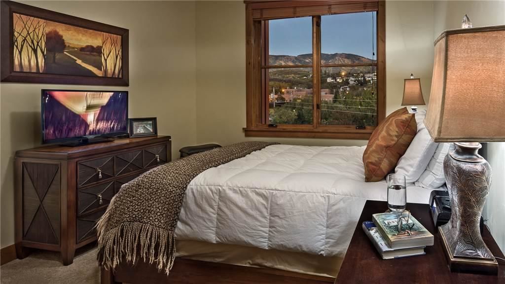 A bedroom with a bed, a TV, a lamp, a window with a view, and a wooden cabinet.