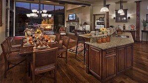 A spacious kitchen with a large island, wooden flooring, and a stone fireplace.