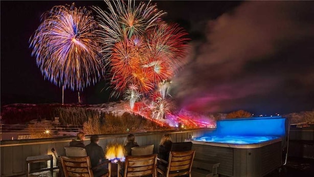 A rooftop bar with outdoor seating and a hot tub, overlooking a fireworks display.