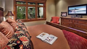 Ein Schlafzimmer mit einem großen Bett, einem Fernseher, einem Schminktisch und einem Fenster mit Blick auf Bäume.