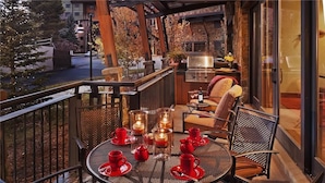 A balcony with a round table set for tea, surrounded by chairs, and a grill area in the background. - Horse Thief Mountain 103 4 BedroomCondo By Moving Mountains (Steamboat Springs)