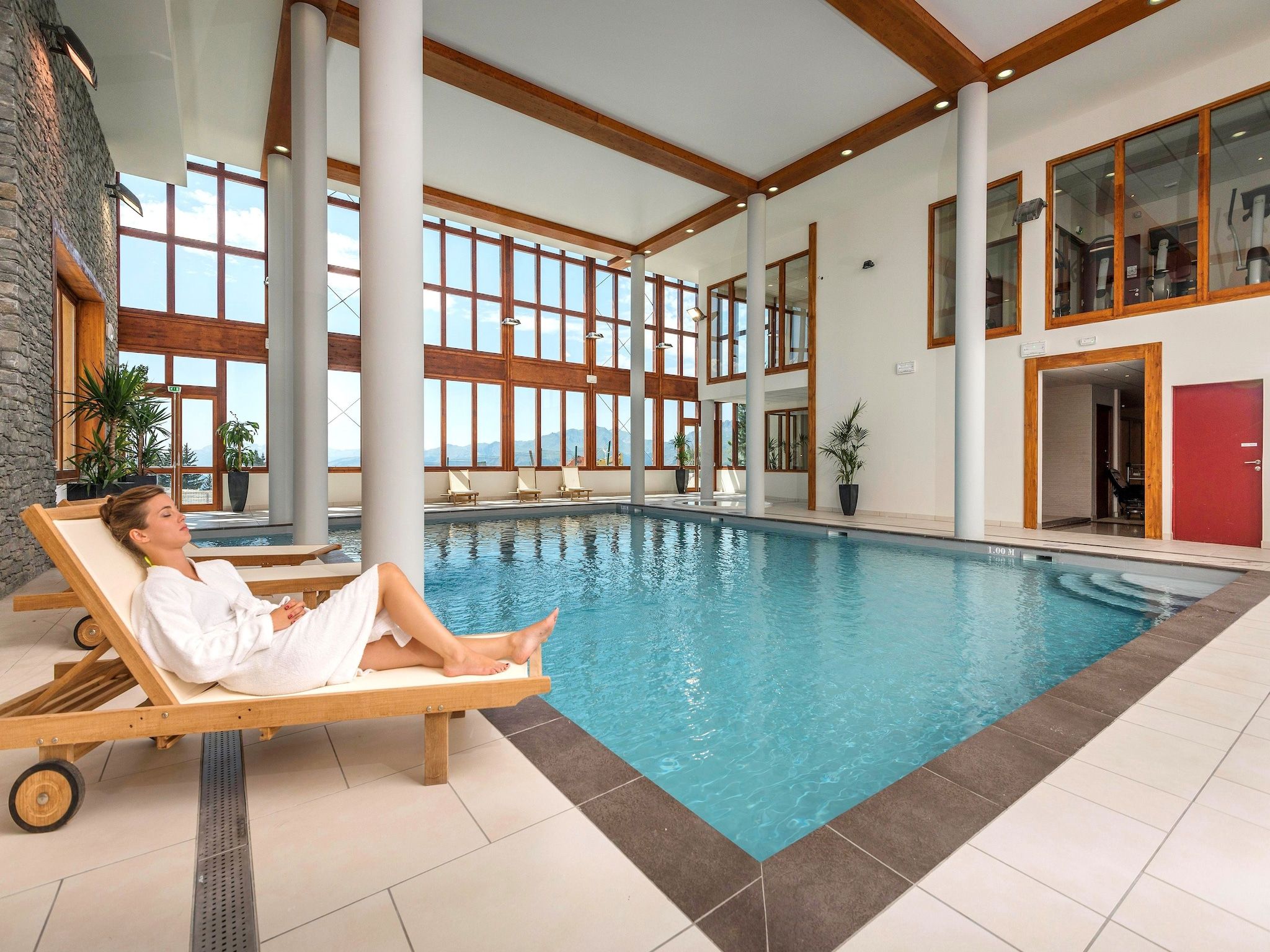 A large indoor swimming pool with a person relaxing on a lounge chair.