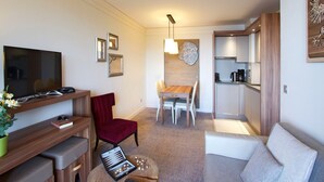 Un espacio habitable compacto con televisión de pantalla plana, una silla roja, una mesa de comedor y una kitchenette.