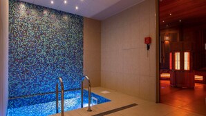 Un área de piscina interior moderna con un muro de mosaicos, una piscina pequeña y una zona de sauna.