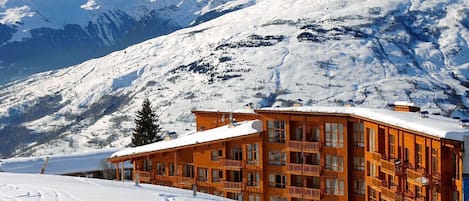 A wooden chalet with multiple balconies, set against a backdrop of snow-covered mountains.