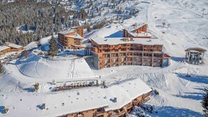 Un complejo turístico en la montaña cubierto de nieve, con varios edificios, pistas de esquí y un cielo despejado.