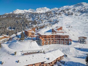 Ein verschneites Bergresort mit mehreren Gebäuden, Skipisten und blauem Himmel.
