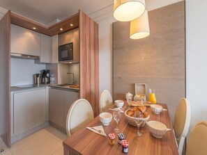 A modern kitchen with a microwave, coffee maker, and toaster. There is a dining table set with plates, bowls, and a basket of croissants.