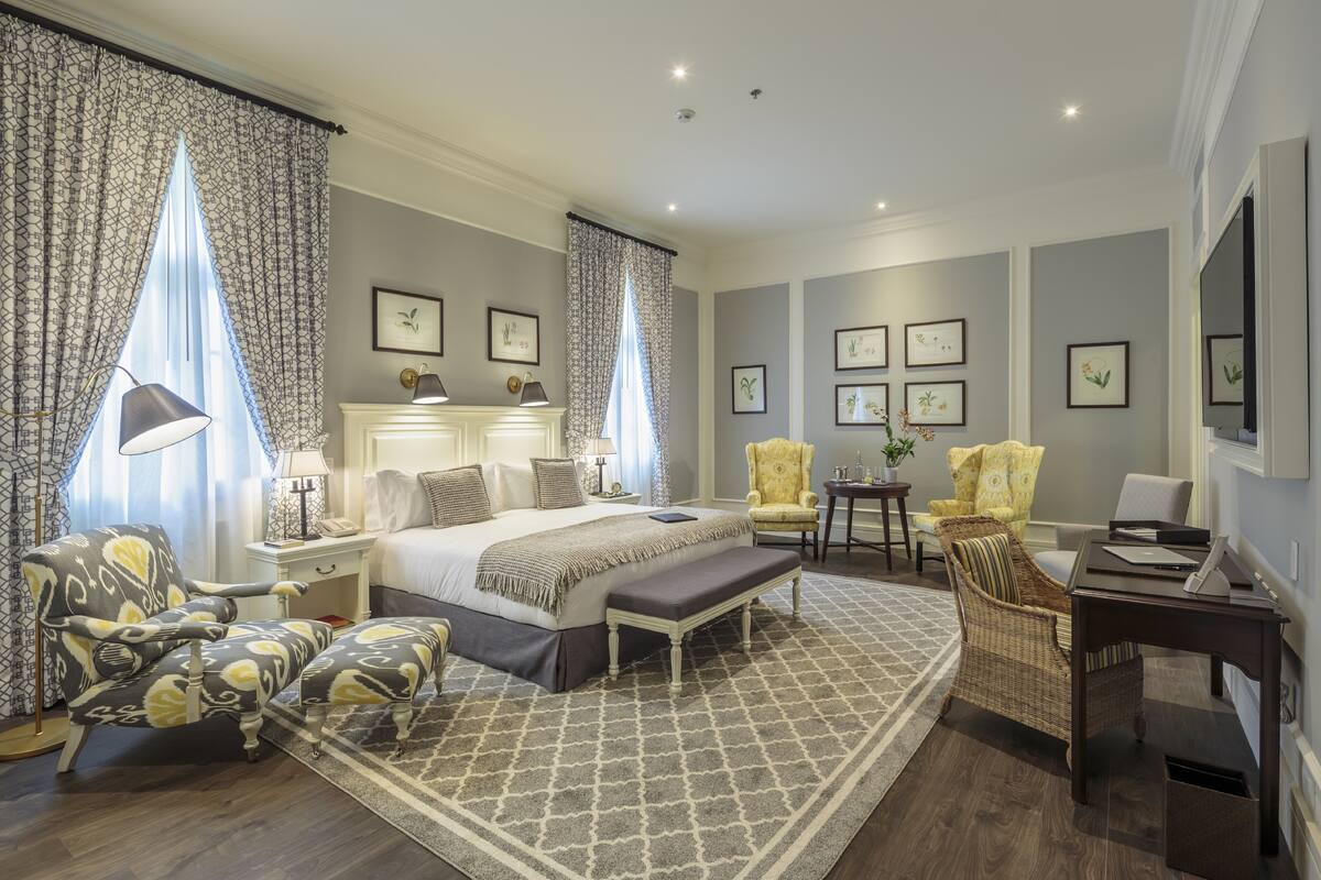 A hotel room with a large bed, two armchairs, a desk, and a small table.
