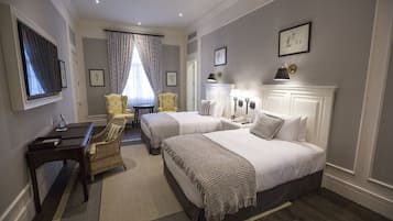 A hotel room with two beds, a desk, a chair, a TV, and a window with curtains.