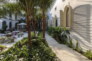 A courtyard with a paved walkway, potted plants, and a building with arched windows and shutters.