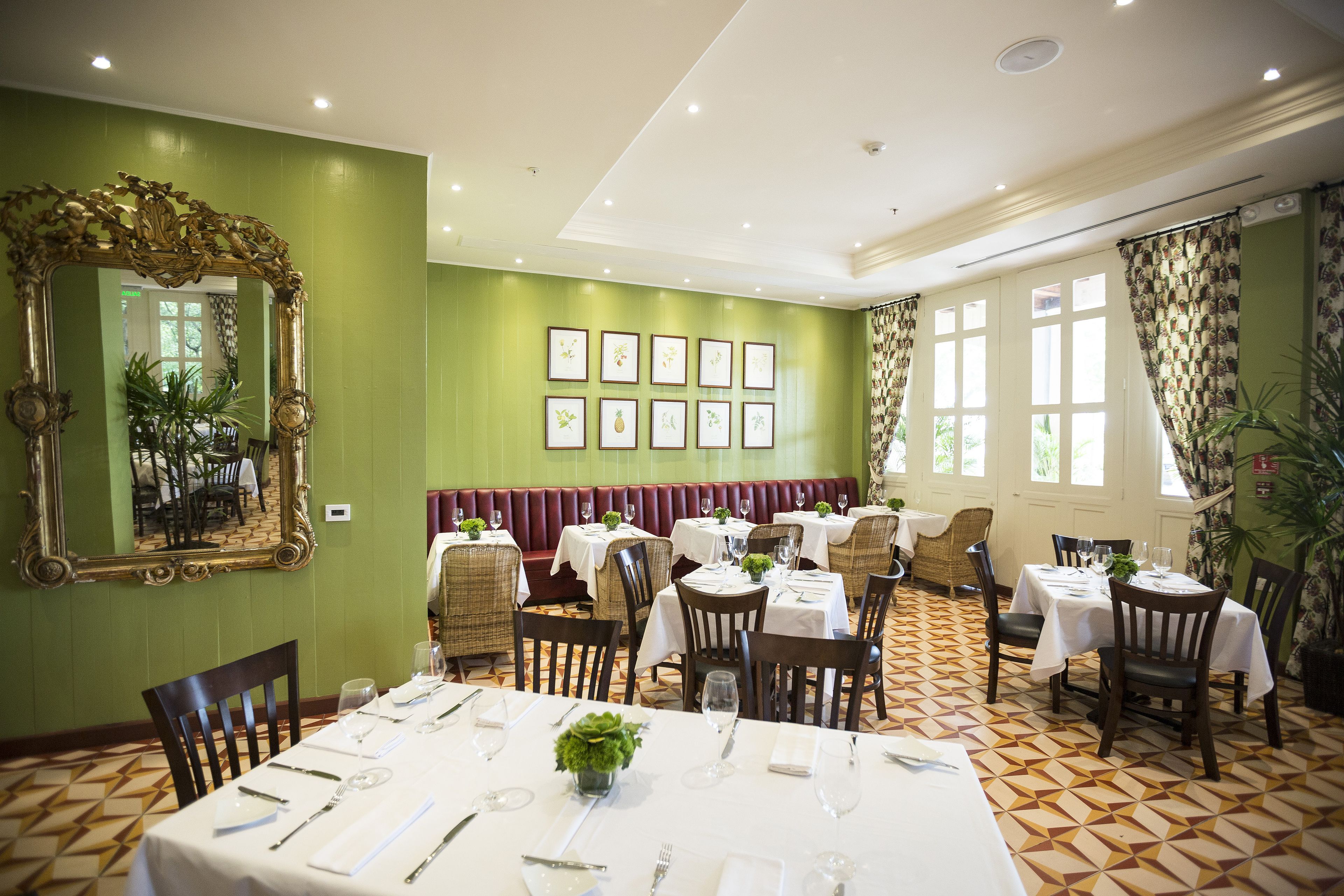 Un comedor con mesas dispuestas para el servicio, un espejo grande y ornamentado, y obras de arte enmarcadas en la pared.