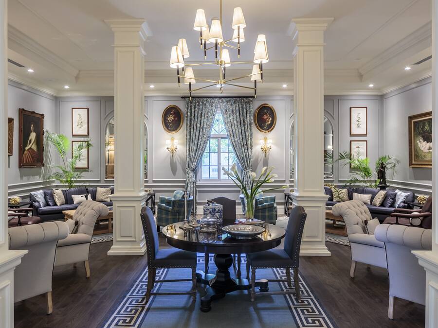Une salle à manger élégante, ornée d’un lustre, comprenant une table ronde et deux canapés avec des coussins.