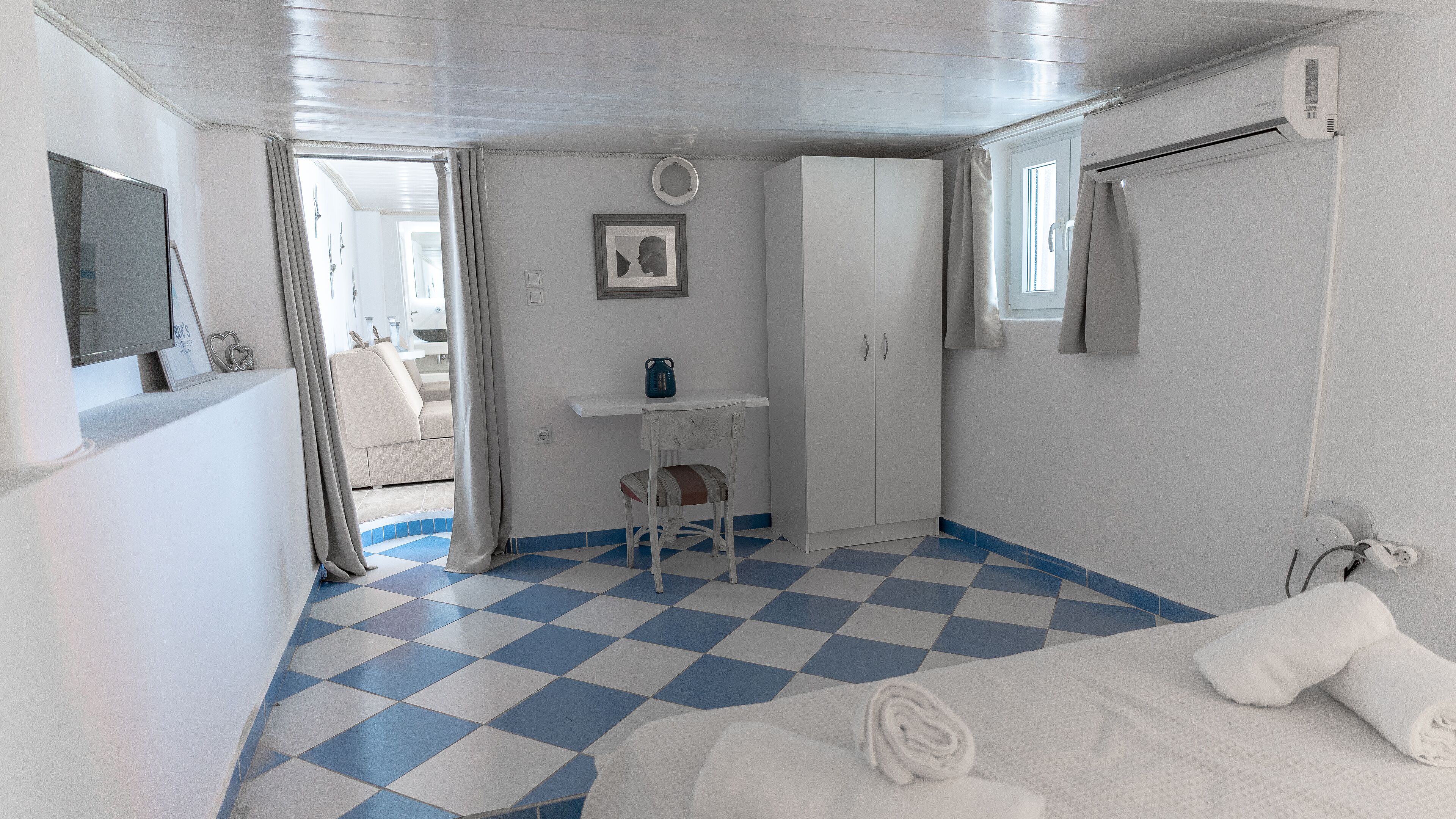 Une pièce avec un sol à carreaux, un lit avec des serviettes, un bureau, une chaise, une armoire, un téléviseur et une fenêtre avec des rideaux.