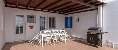 A covered patio with a table and chairs, a grill, and a white door.