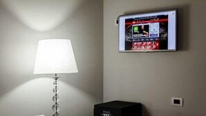 Ett rum med en väggmonterad platt-TV som visar en sportkanal, en modern lampa och en liten svart elektronisk apparat på ett bord.