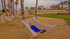 Una hamaca en una playa arenosa con palmeras, cielo despejado y vista al océano.